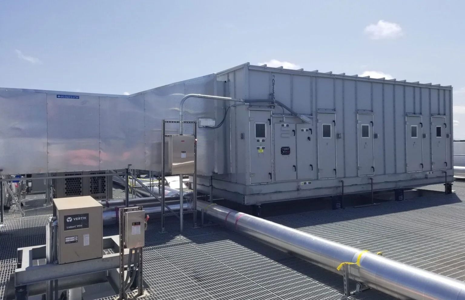 A large industrial HVAC unit sits on a grey rooftop under a bright blue sky.