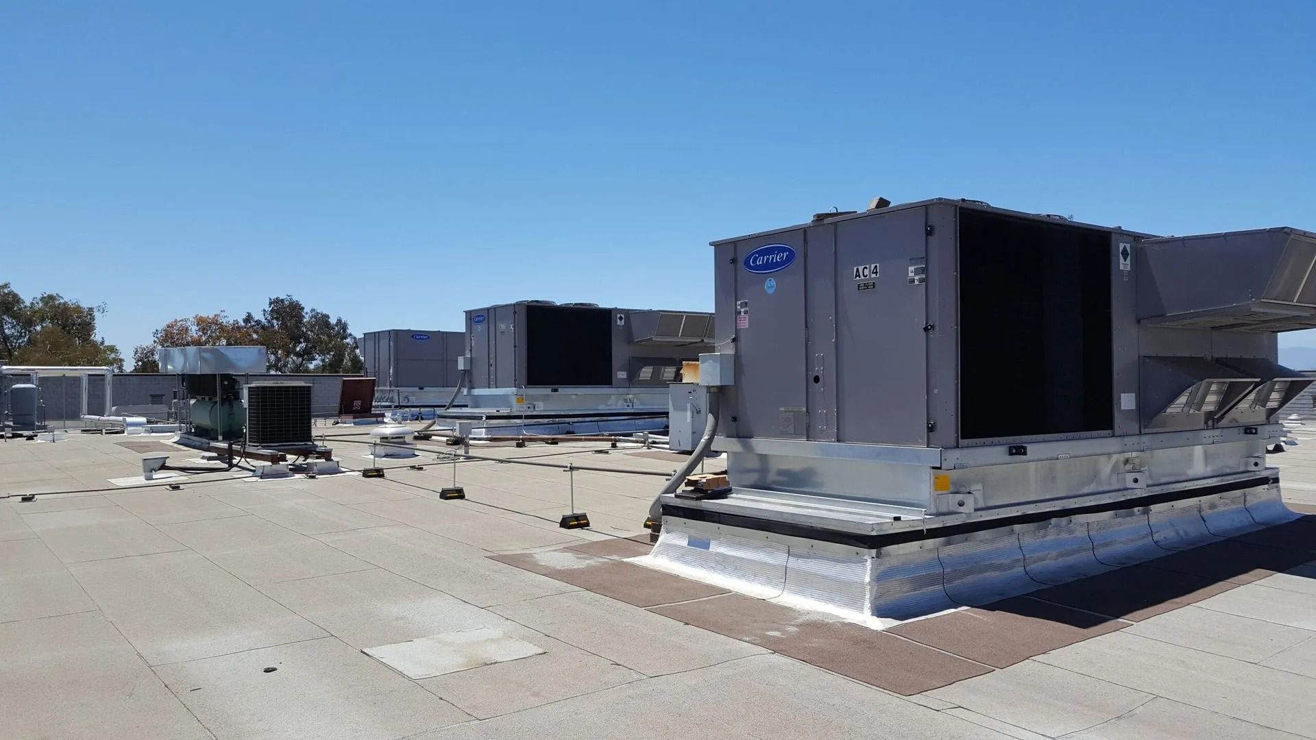 Several large HVAC rooftop units installed on a flat, industrial gravel roof under a clear blue sky.