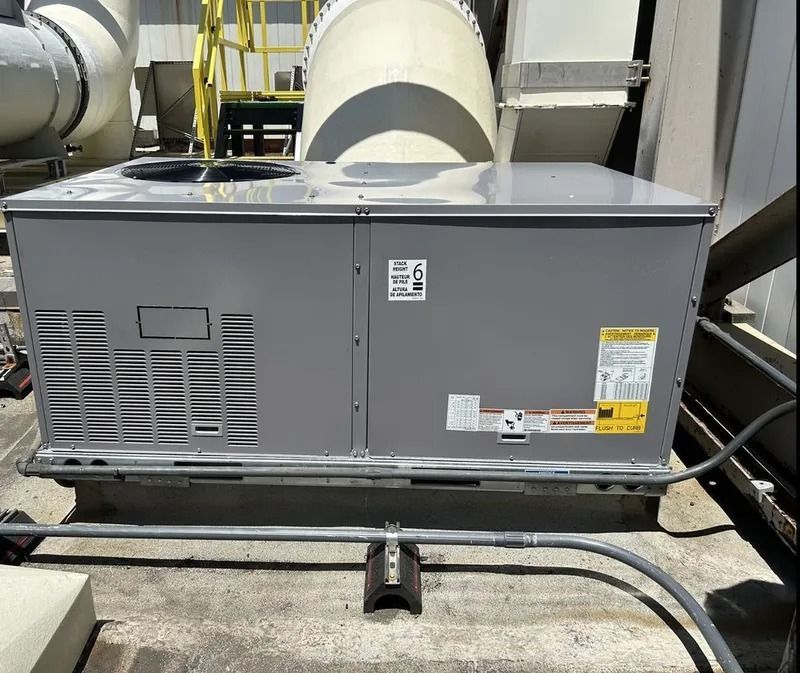 A gray HVAC unit sits on a rooftop next to metal ductwork and a ladder structure under bright sunlight.