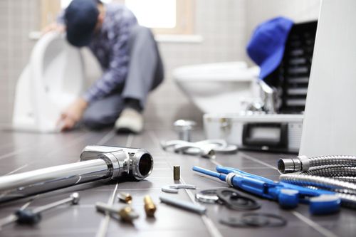 Plumber’s tools on a floor with a worker repairing pipes in the blurred background
