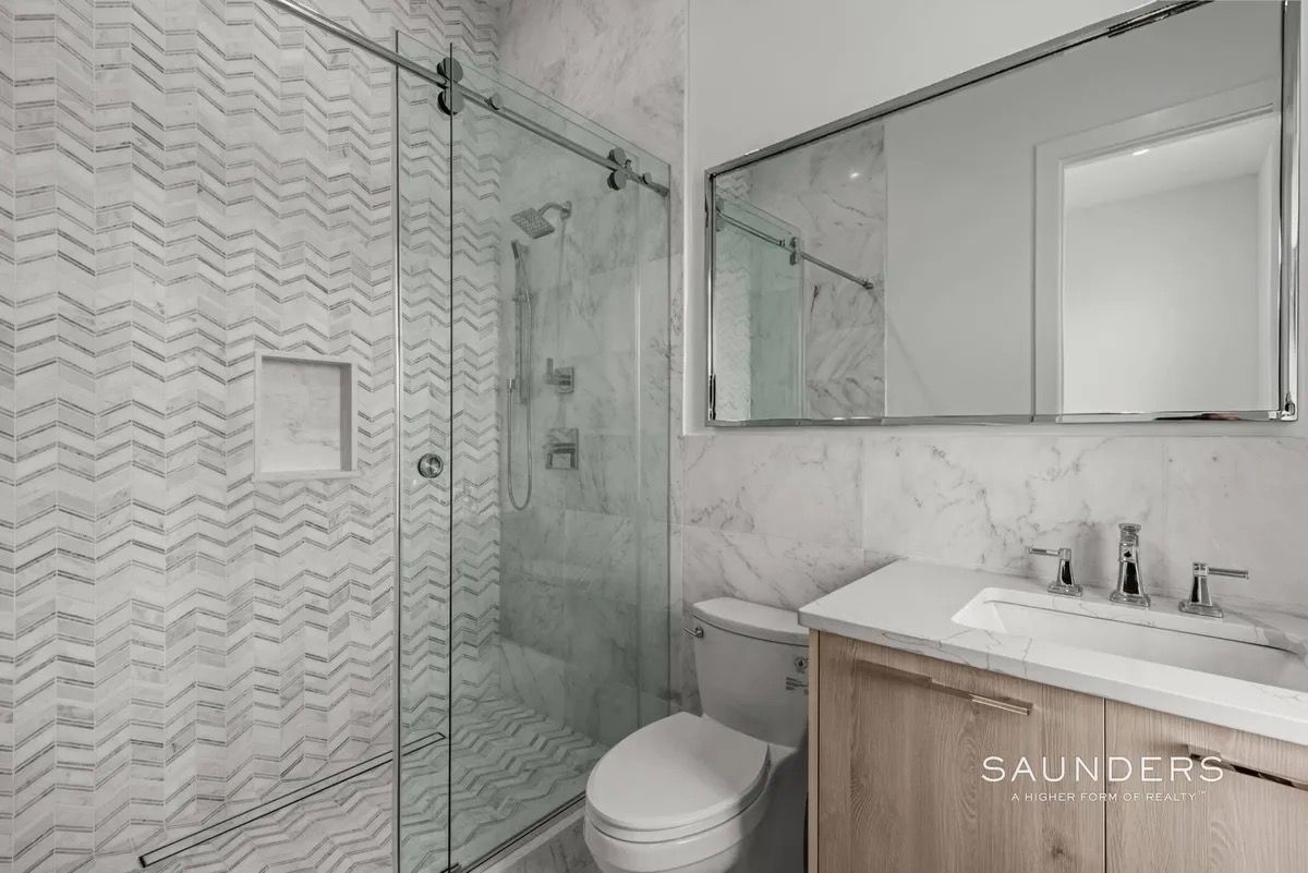Modern bathroom with glass shower, white chevron tile, toilet, and wood vanity with mirror.