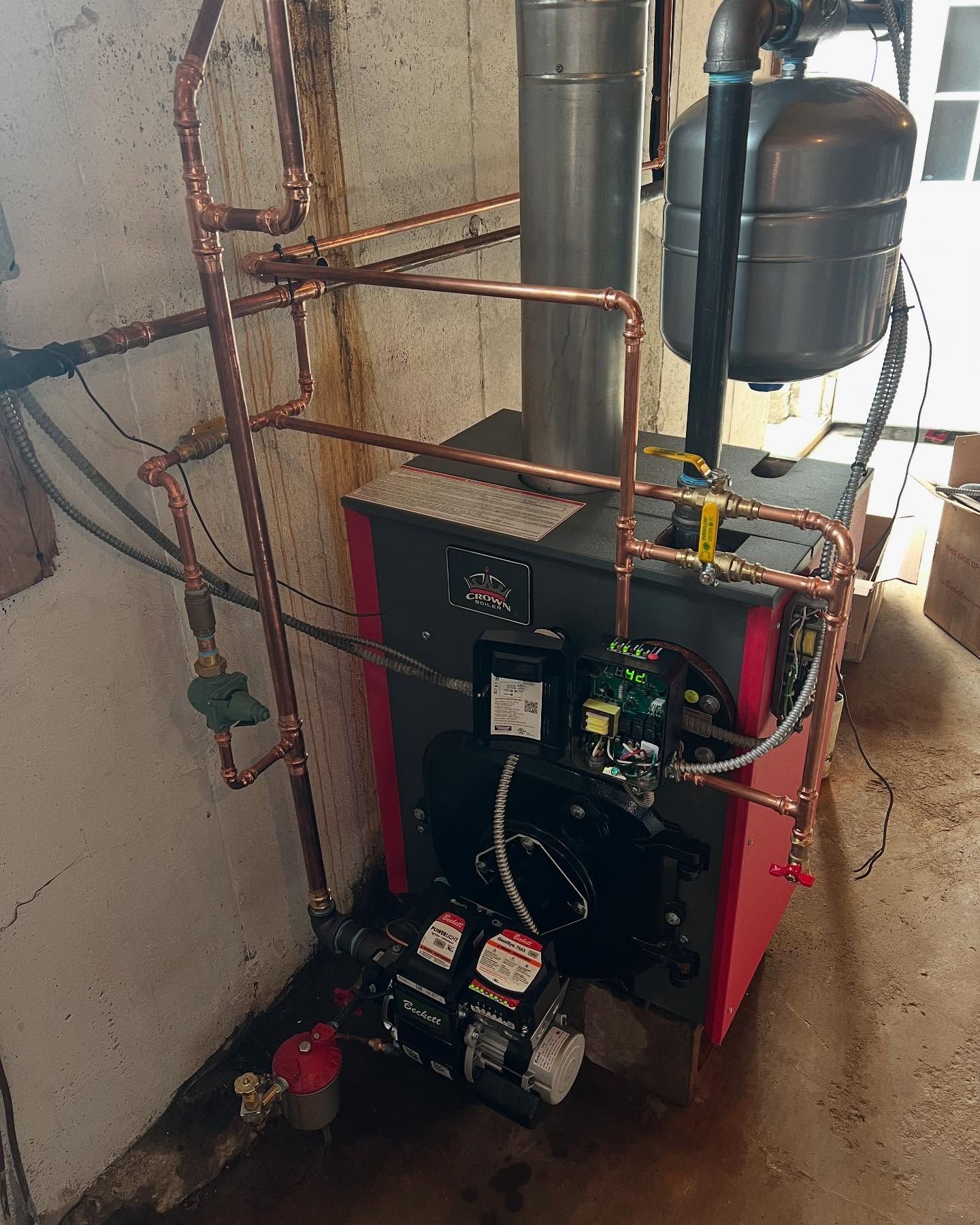Boiler room with red heating unit, pipes, pressure tank, and pumps against a concrete wall.
