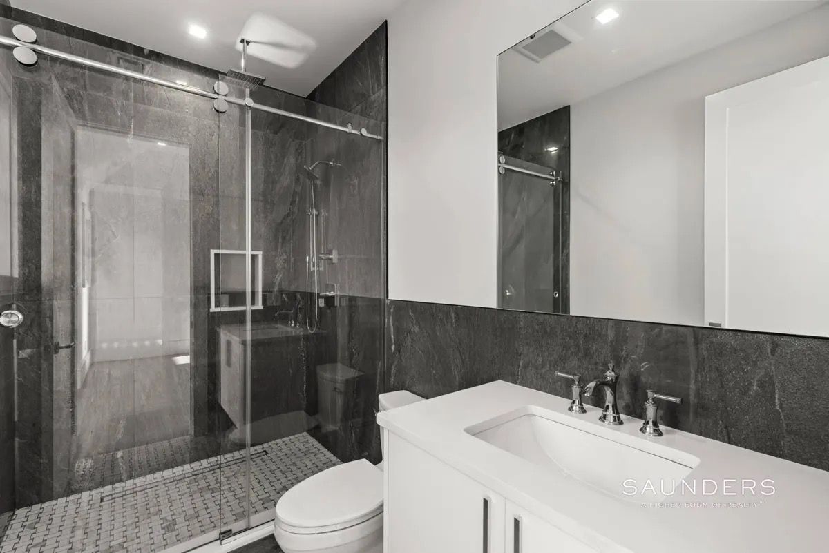 Modern bathroom with glass shower, dark tile, white vanity, and toilet.