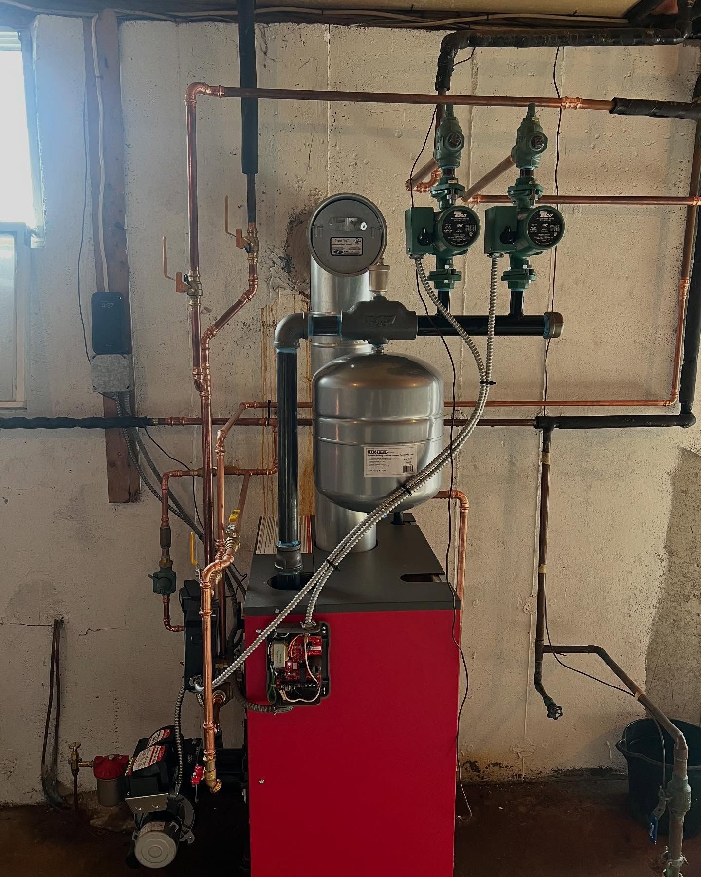 Basement utility room with boiler, pressure tank, pipes, gauges, and valves on a red cabinet