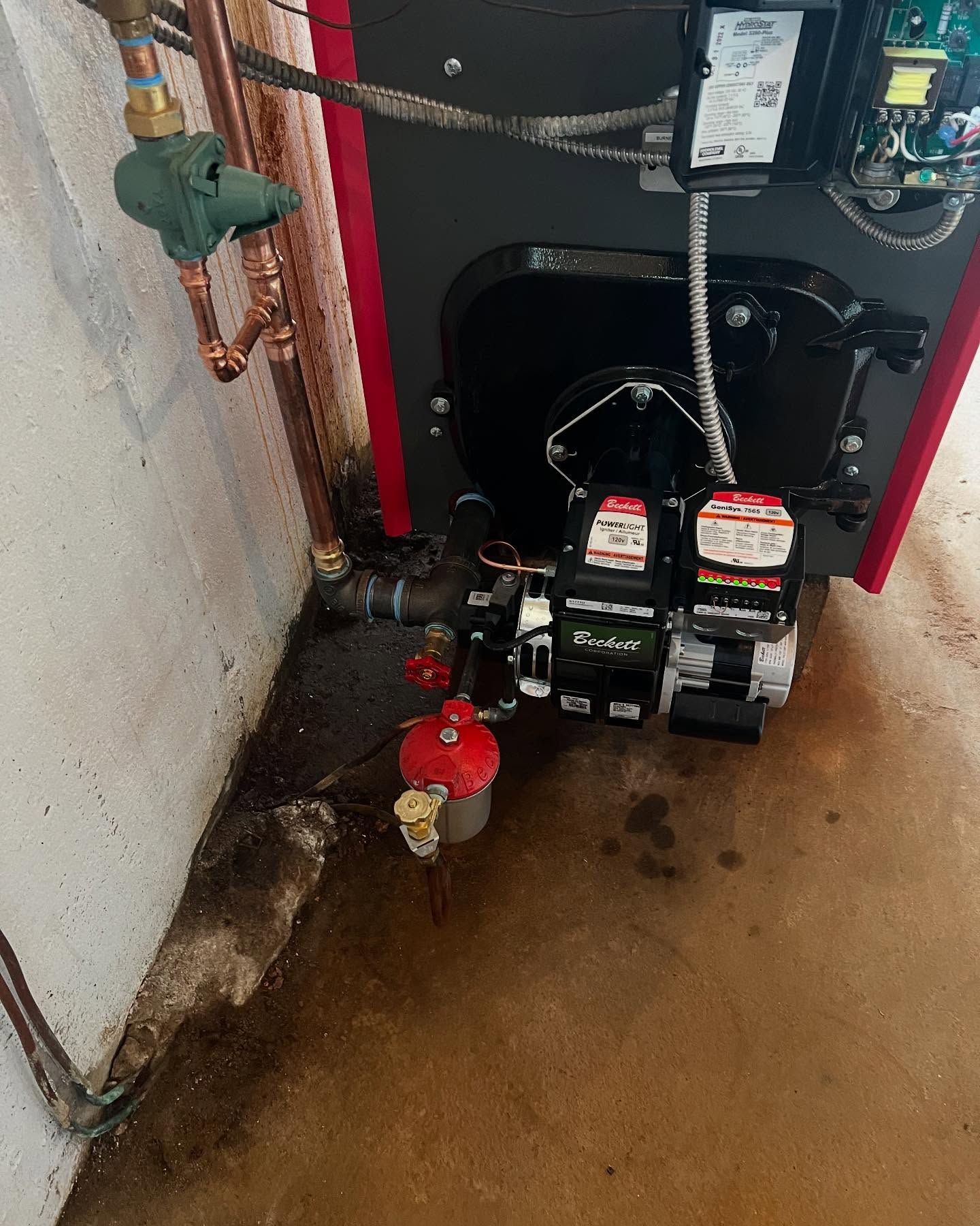 Utility meters and red gas shutoff valve in a narrow basement corner with damp concrete floor