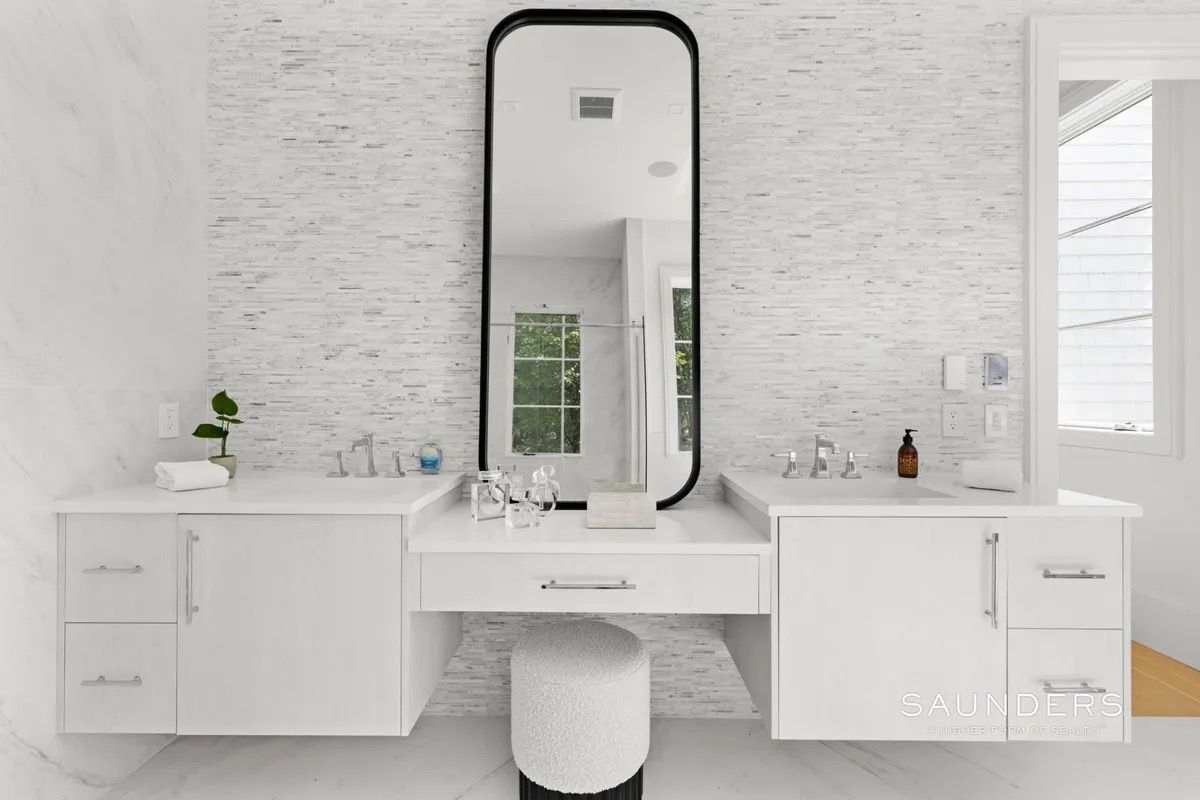 Bright white bathroom vanity with large mirror, double sinks, and a small stool in a modern minimalist space