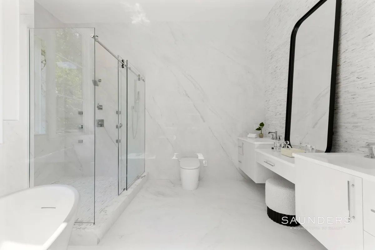 Minimalist white bathroom with glass shower, freestanding tub, toilet, and long double vanity