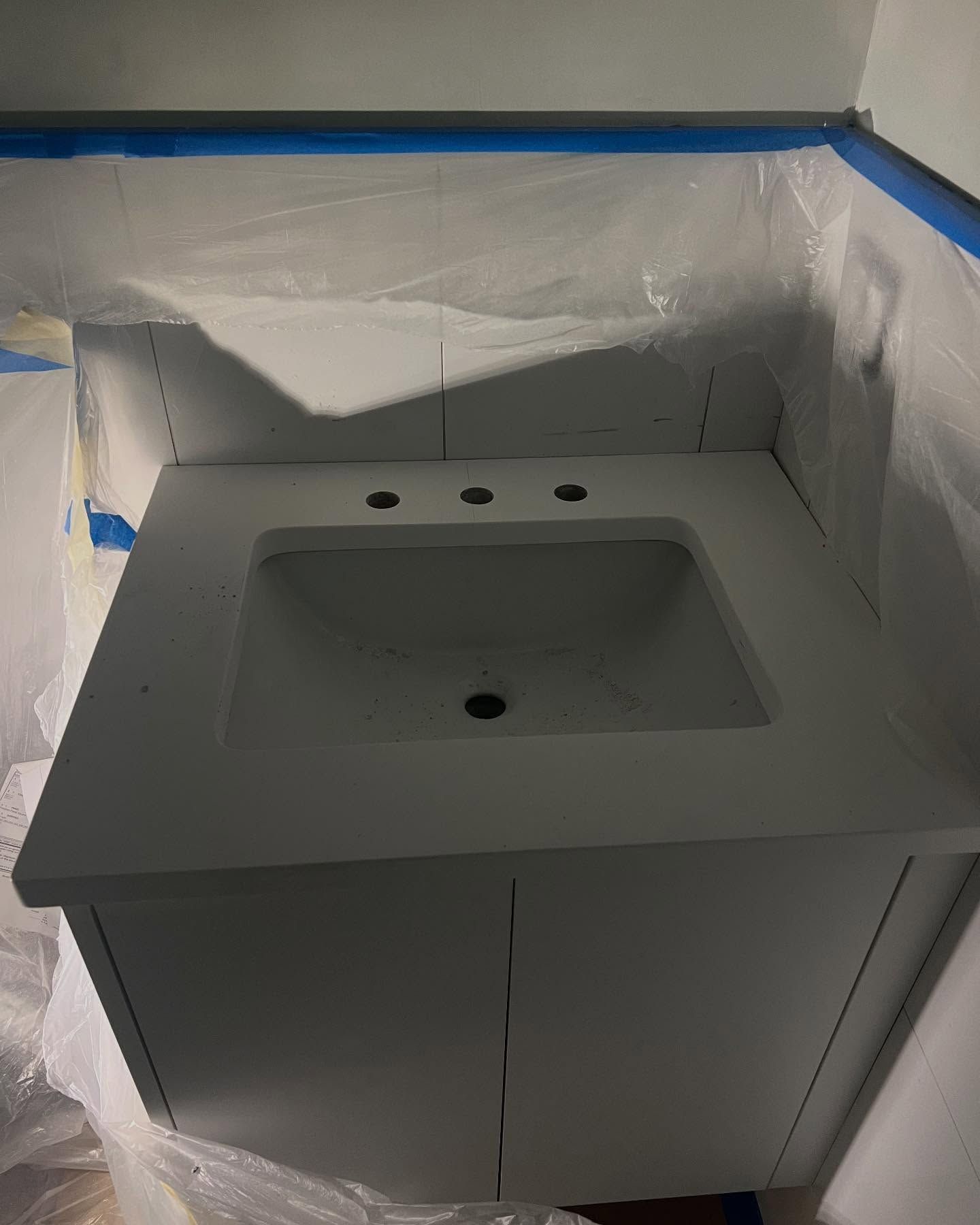Bathroom vanity with sink and three faucet holes, masked with blue tape during painting.