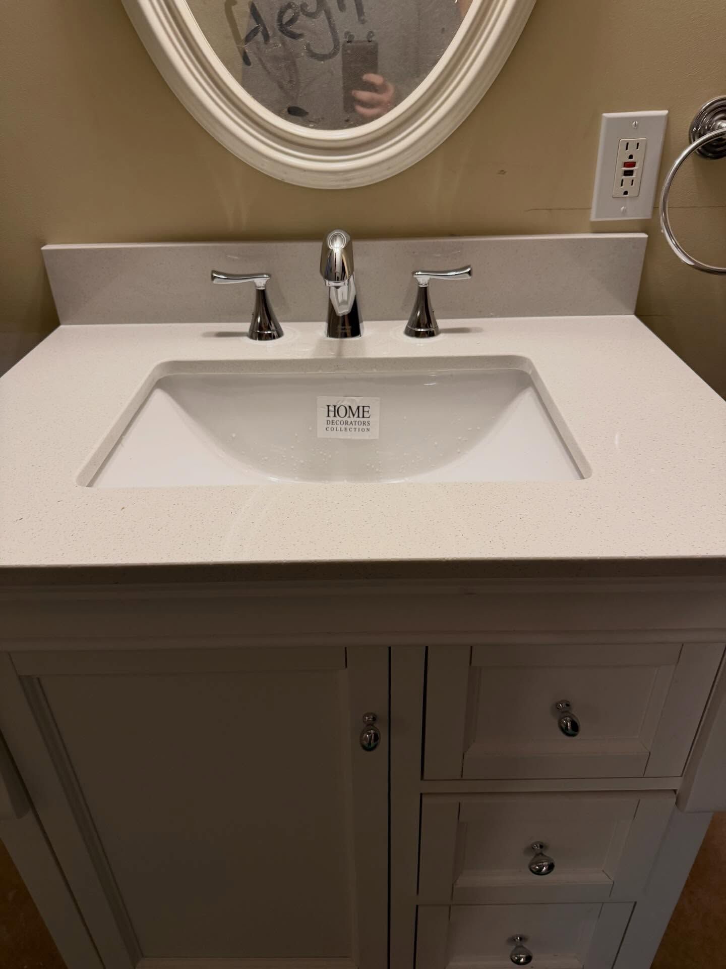 Bathroom vanity with white sink, chrome faucet, and mirror above a beige countertop.