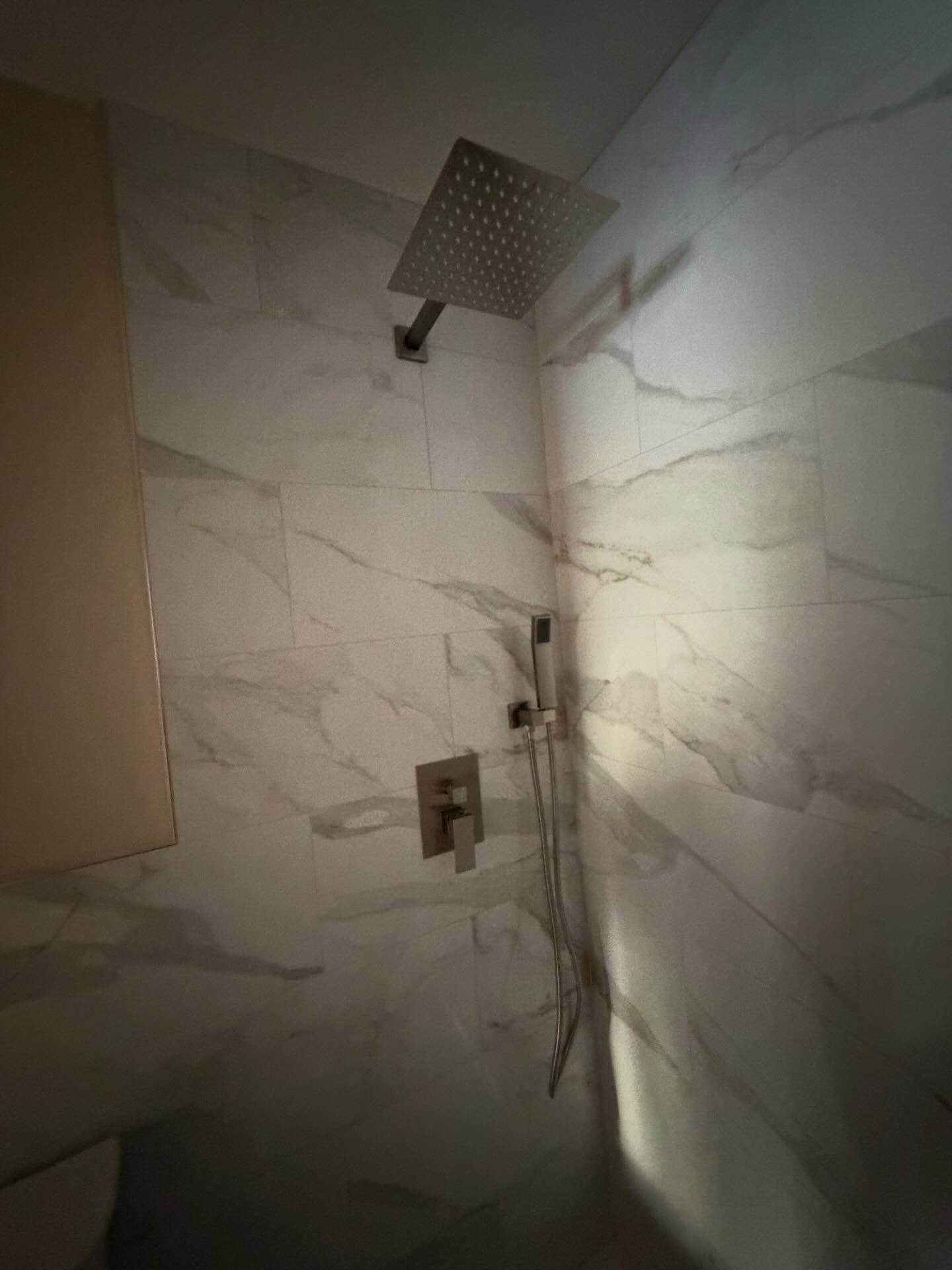 Tile shower with wall-mounted square rainfall showerhead and handheld shower fixture