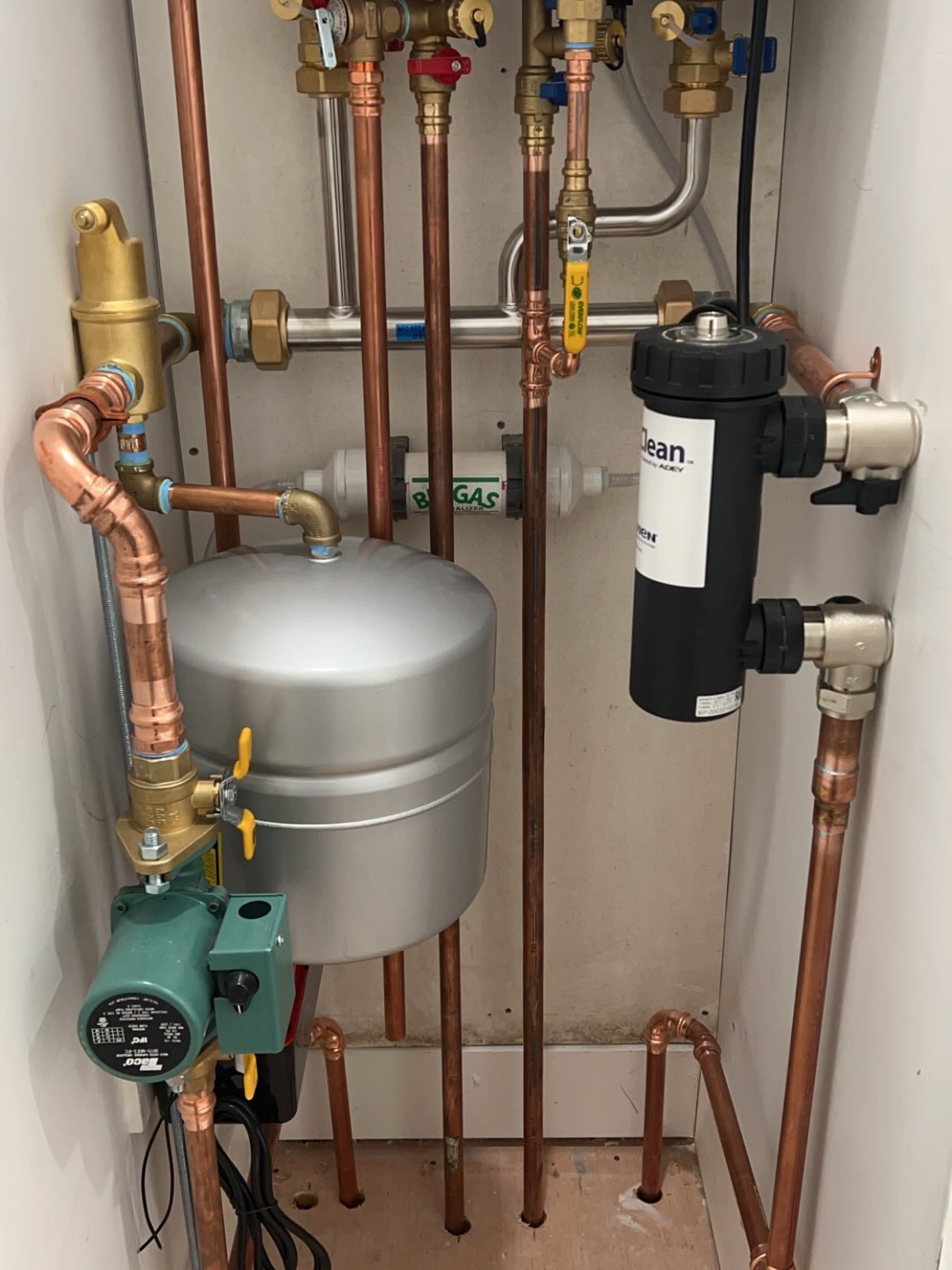 Plumbing and heating equipment with copper pipes, valves, a silver tank, and a black water filter in a utility closet