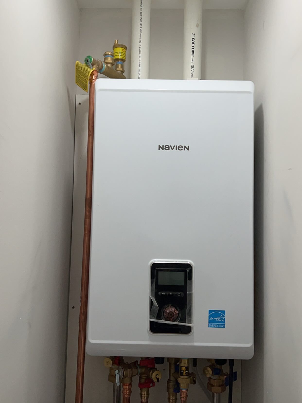 White wall-mounted gas boiler in a utility room with pipes and fittings below.