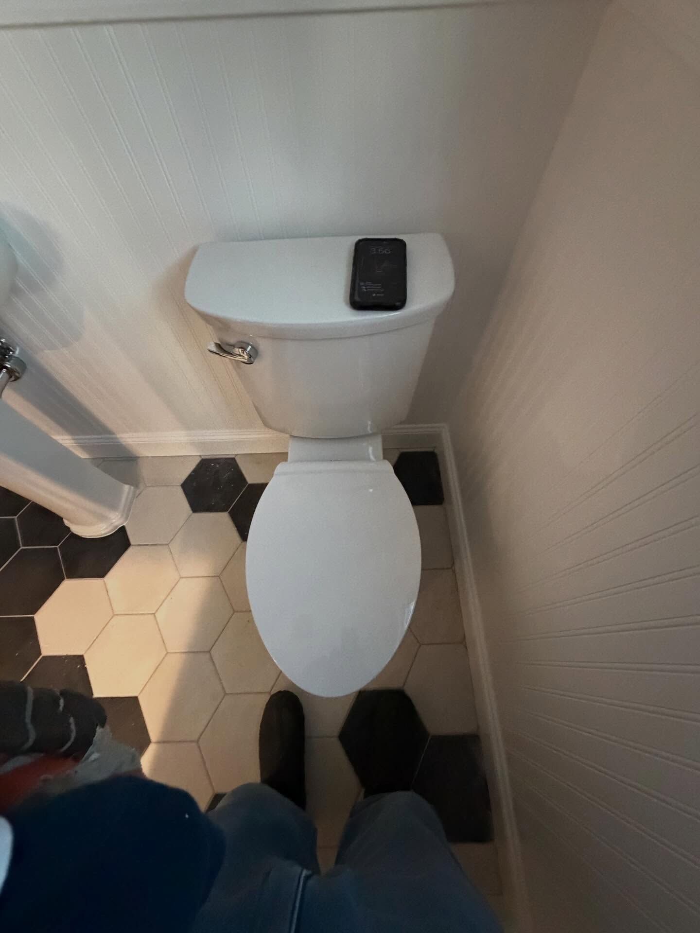 Small bathroom with a white toilet, black-and-white hex tile floor, and a phone on the tank lid.