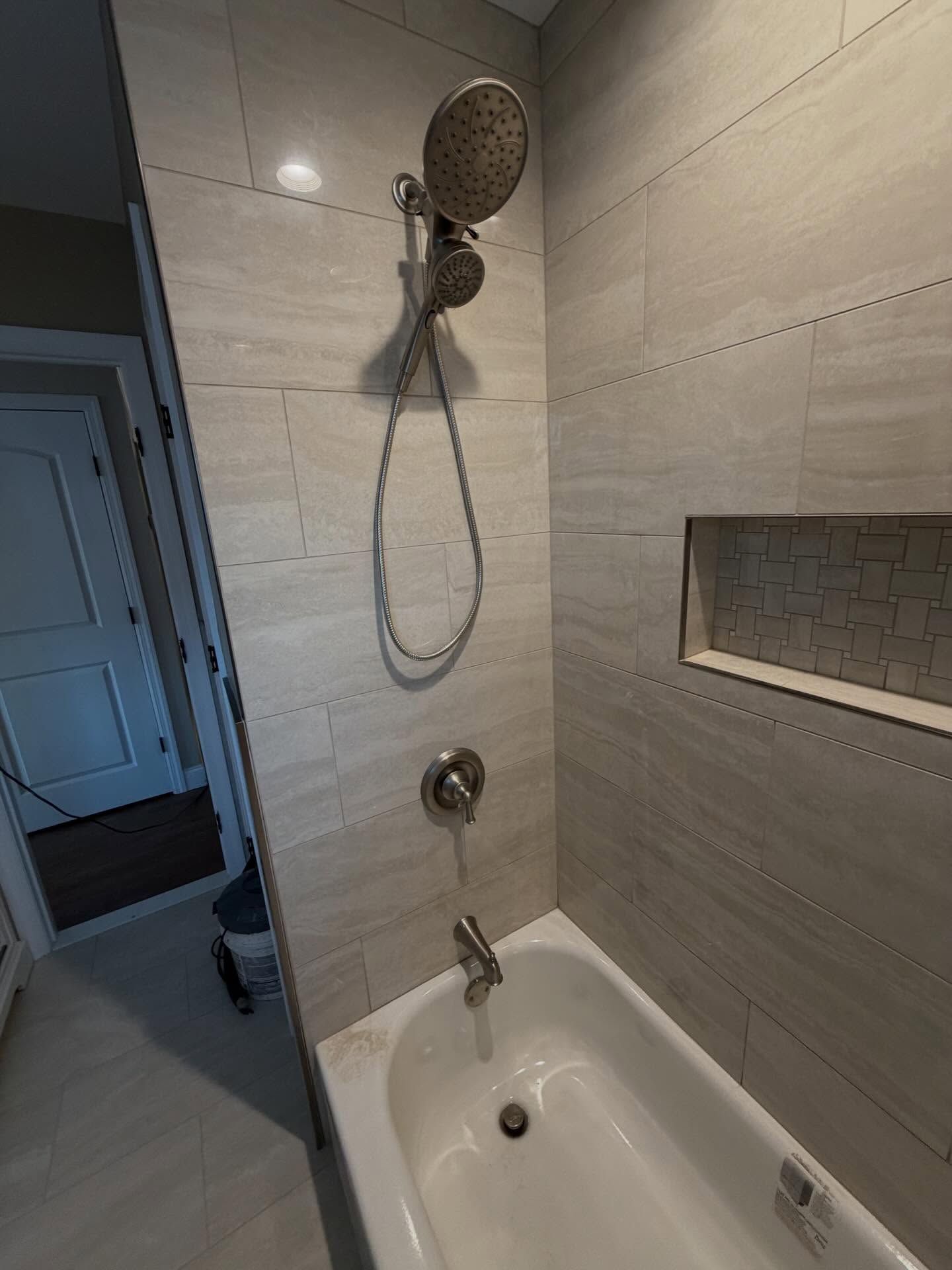 Bathroom shower and tub with handheld showerhead, tiled walls, and a recessed shelf niche.