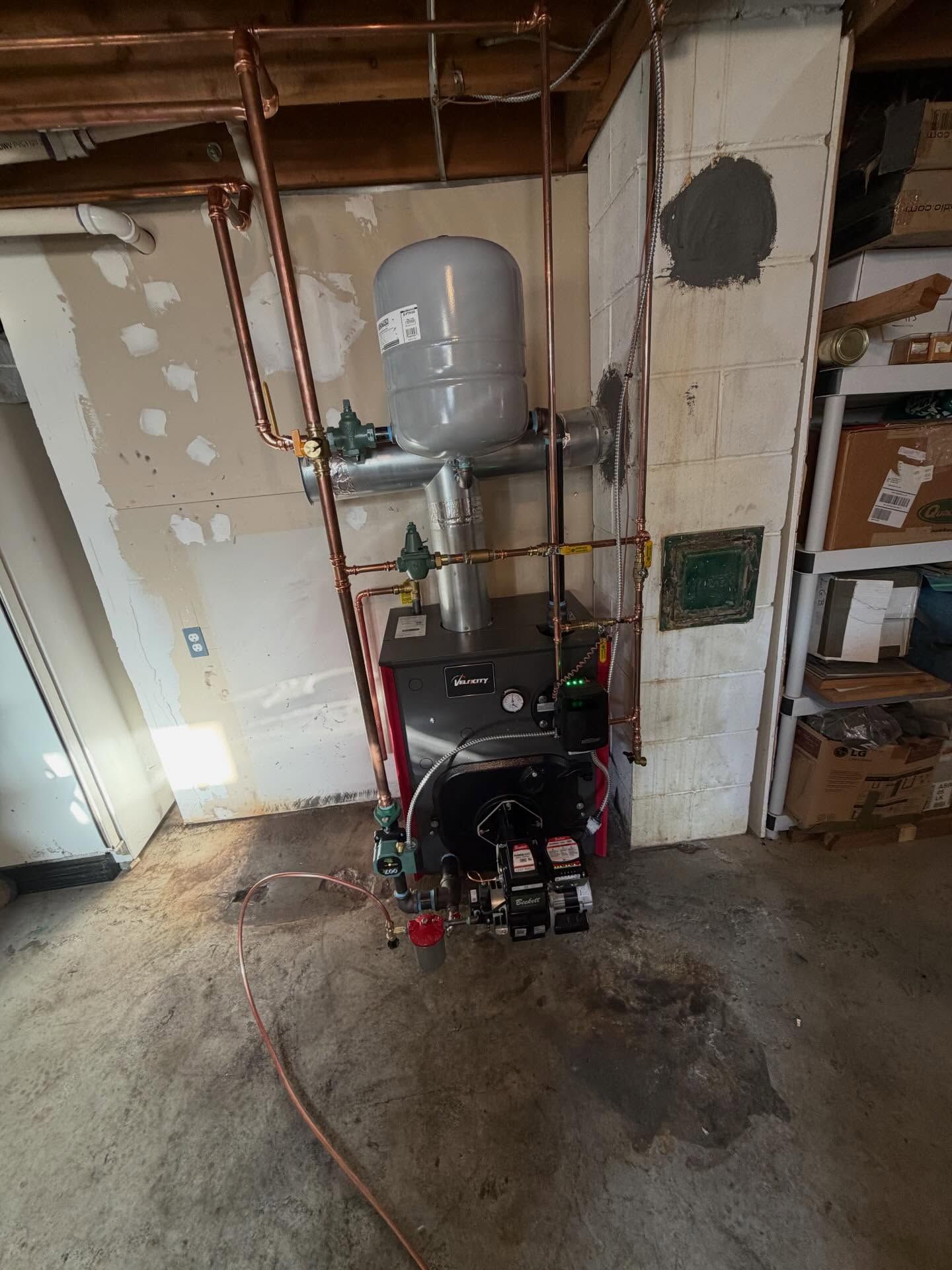 Basement utility area with a boiler, pipes, and a red pressure washer on the concrete floor.
