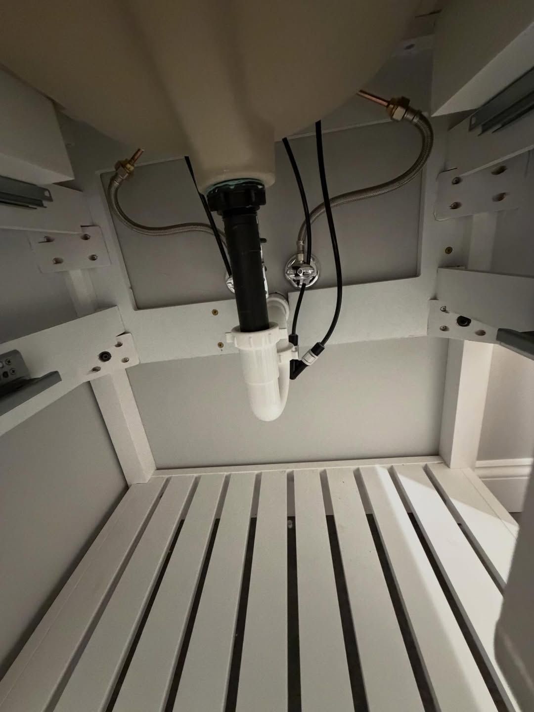 White cabinet interior with a black faucet and visible wires above a slatted shelf