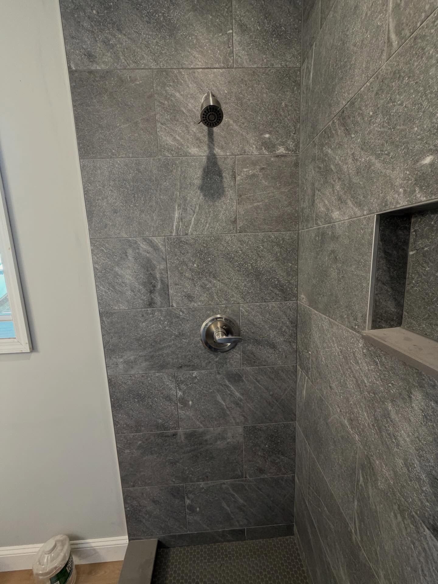 Gray tiled shower wall with two fixtures and a recessed shelf.