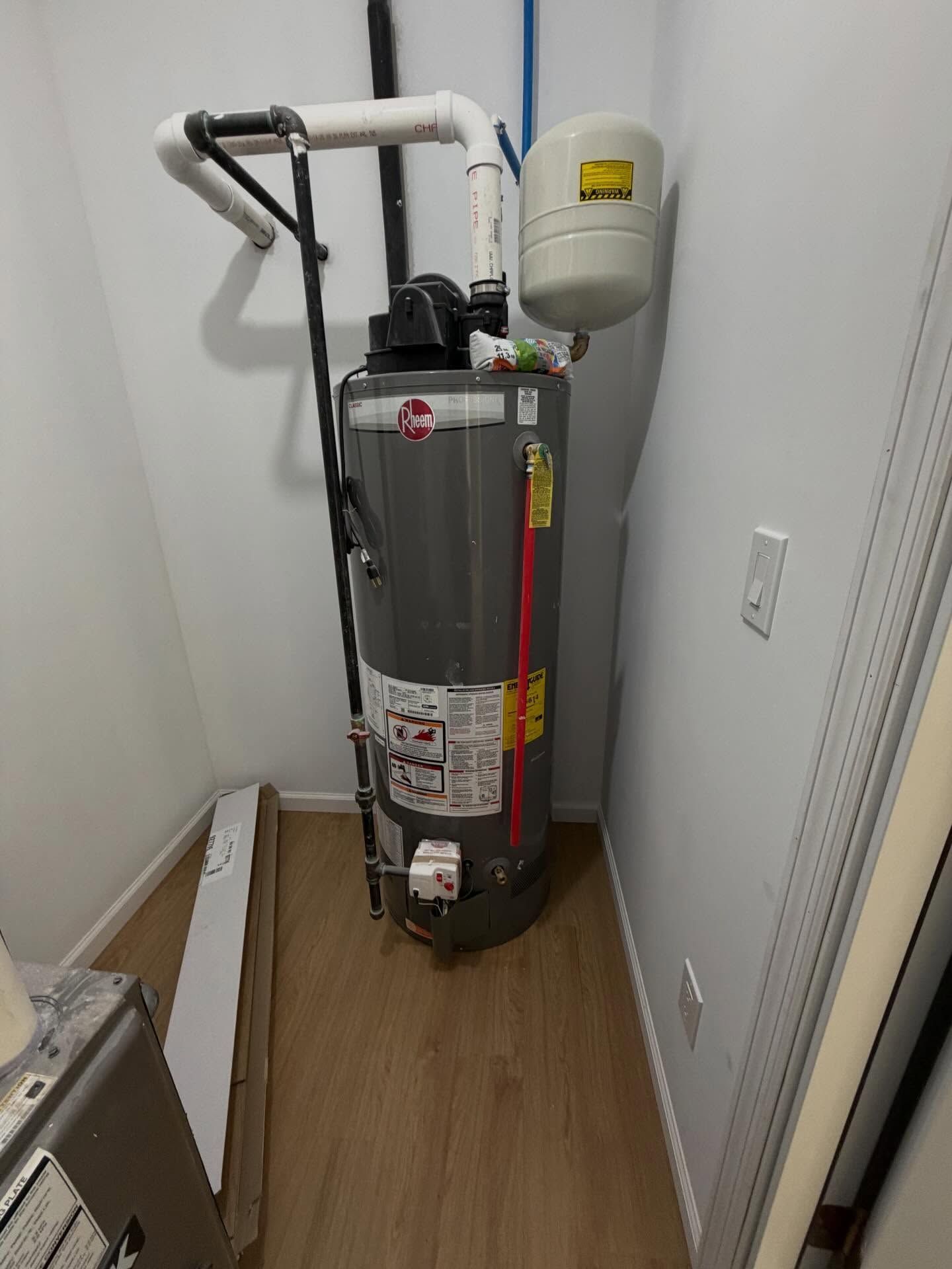 Water heater and expansion tank in a narrow utility closet with wood flooring.