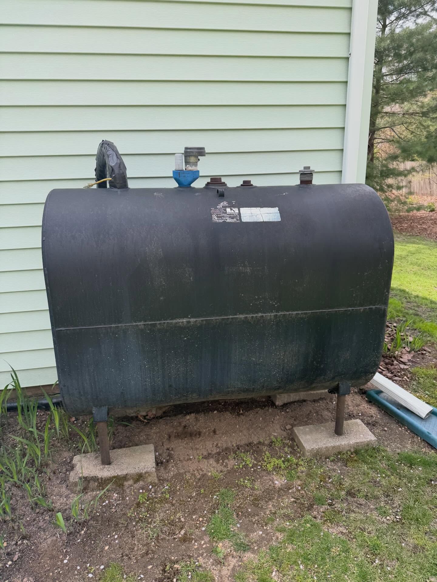 Black cylindrical tank on cinder blocks beside a pale green house wall in a yard