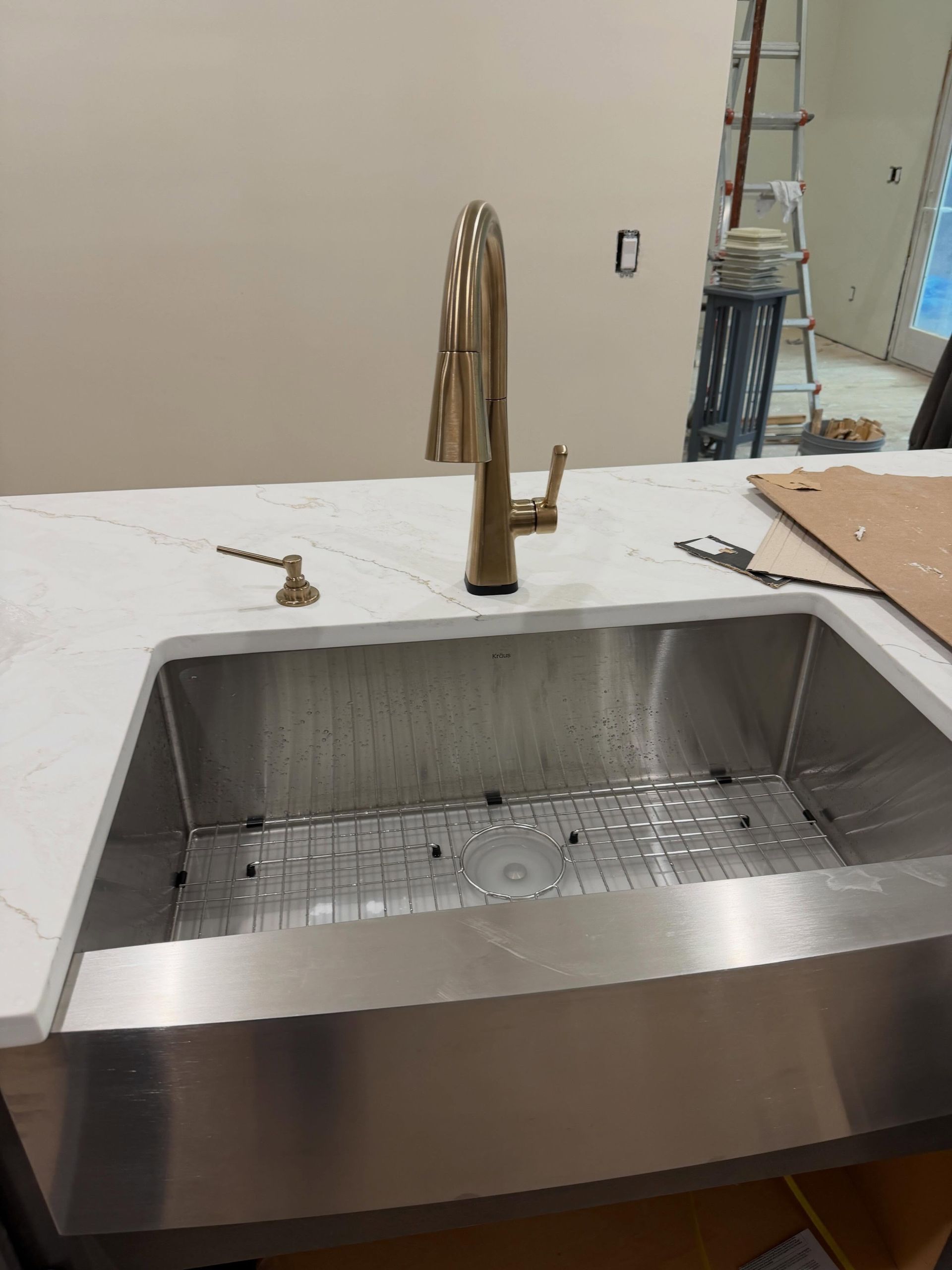 Kitchen sink with brass faucet and white countertop in a room under construction