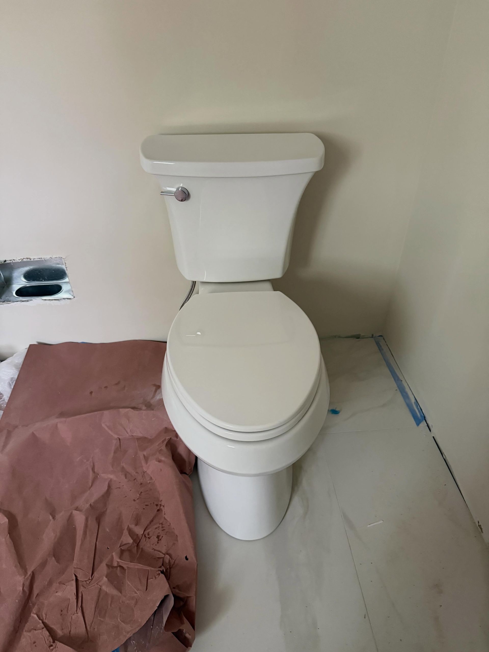 Toilet in a small bathroom under construction, with a pink drop cloth and unfinished walls.