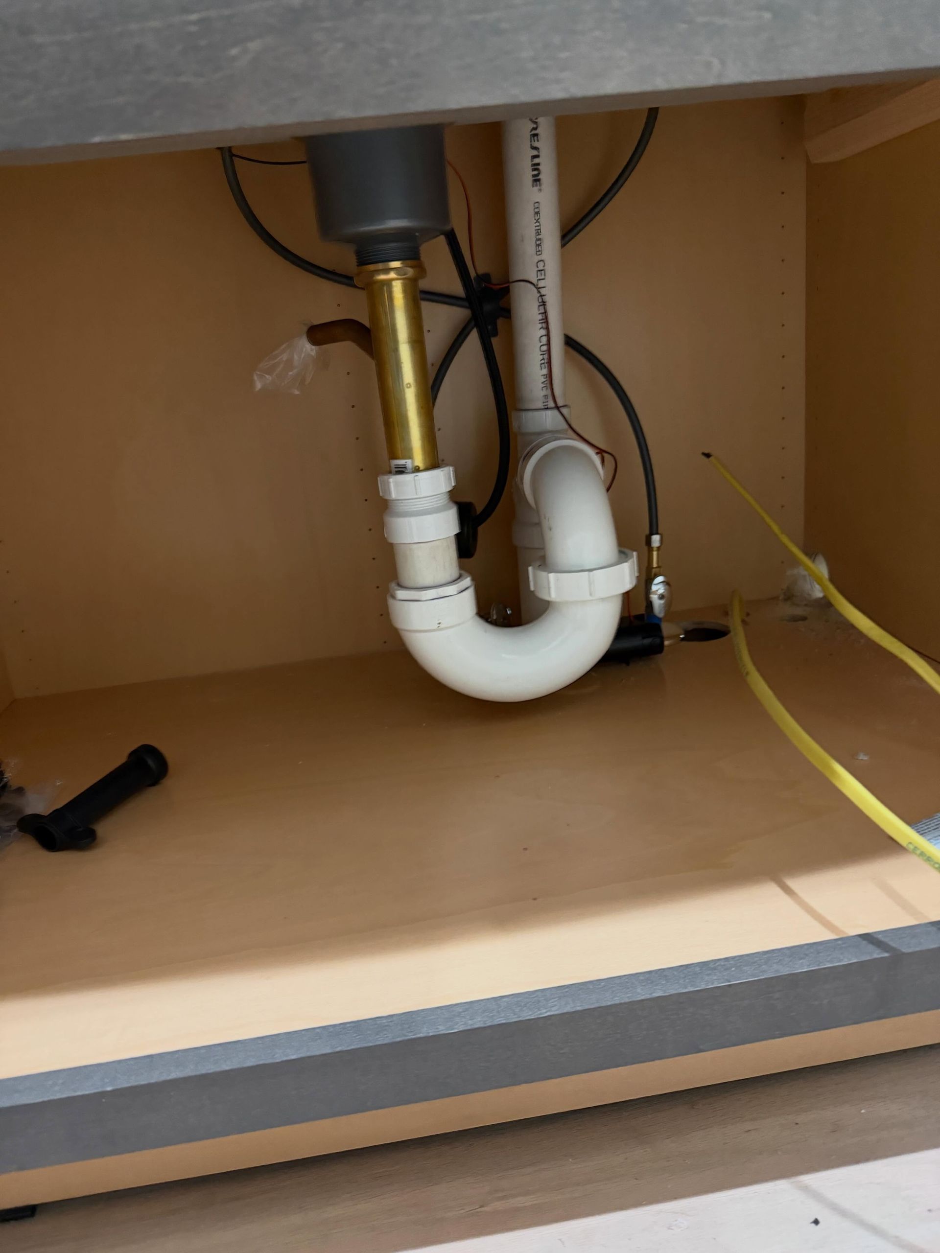 Under-sink plumbing with white P-trap pipes and brass fittings inside a cabinet.