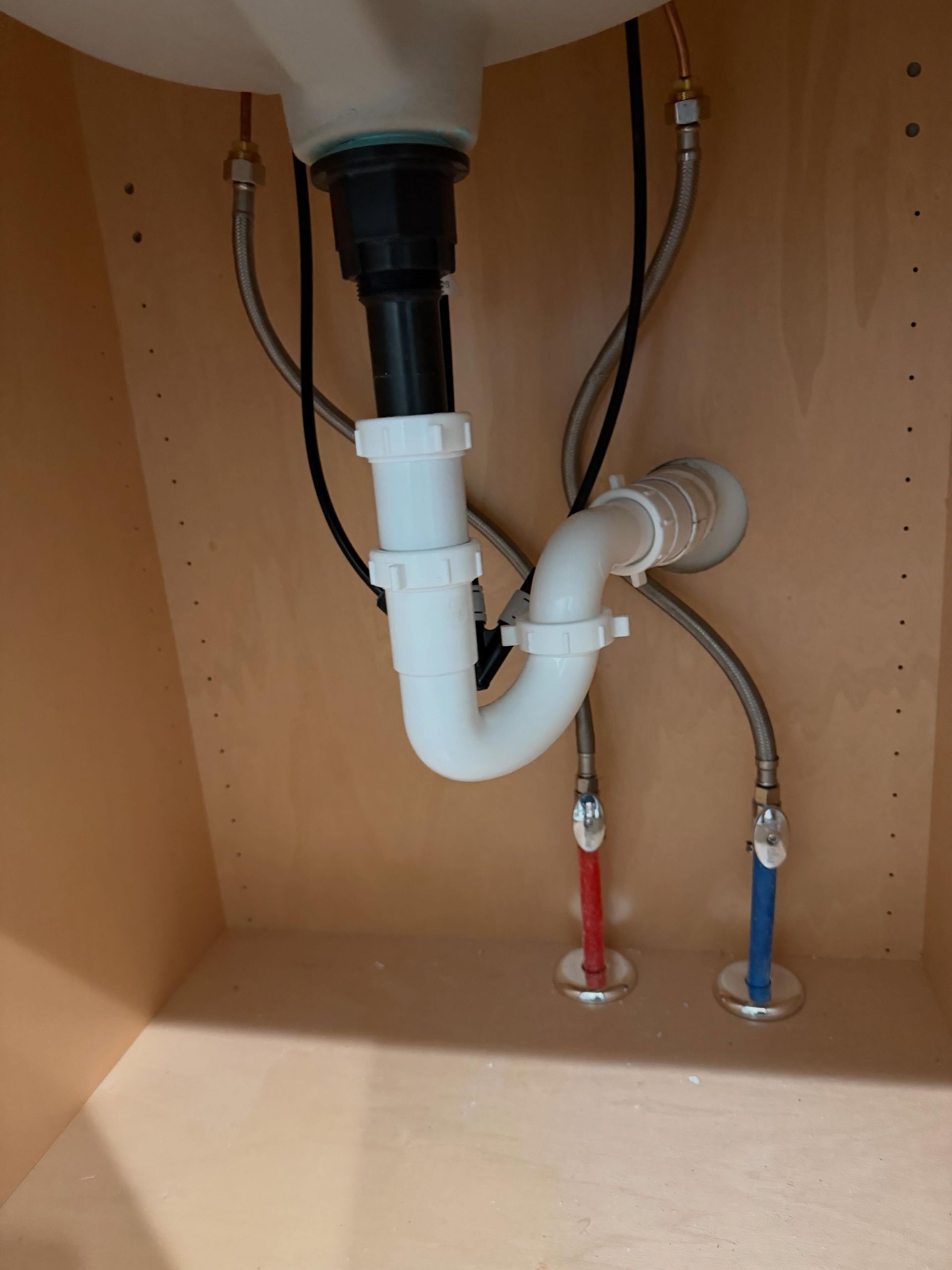 Under-sink plumbing with white drain pipe, black trap, and red and blue water shutoff valves