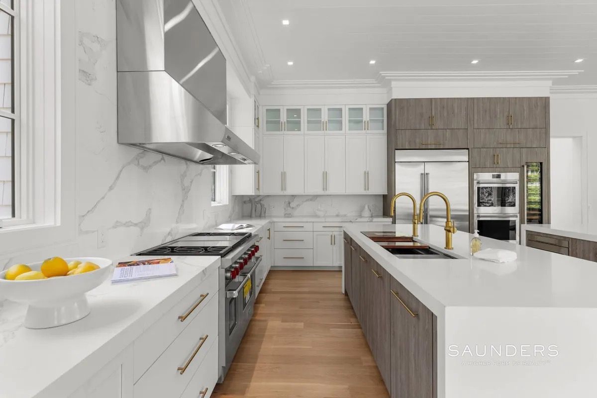 Bright modern white kitchen with wood island, stainless appliances, and gold faucet fixtures.