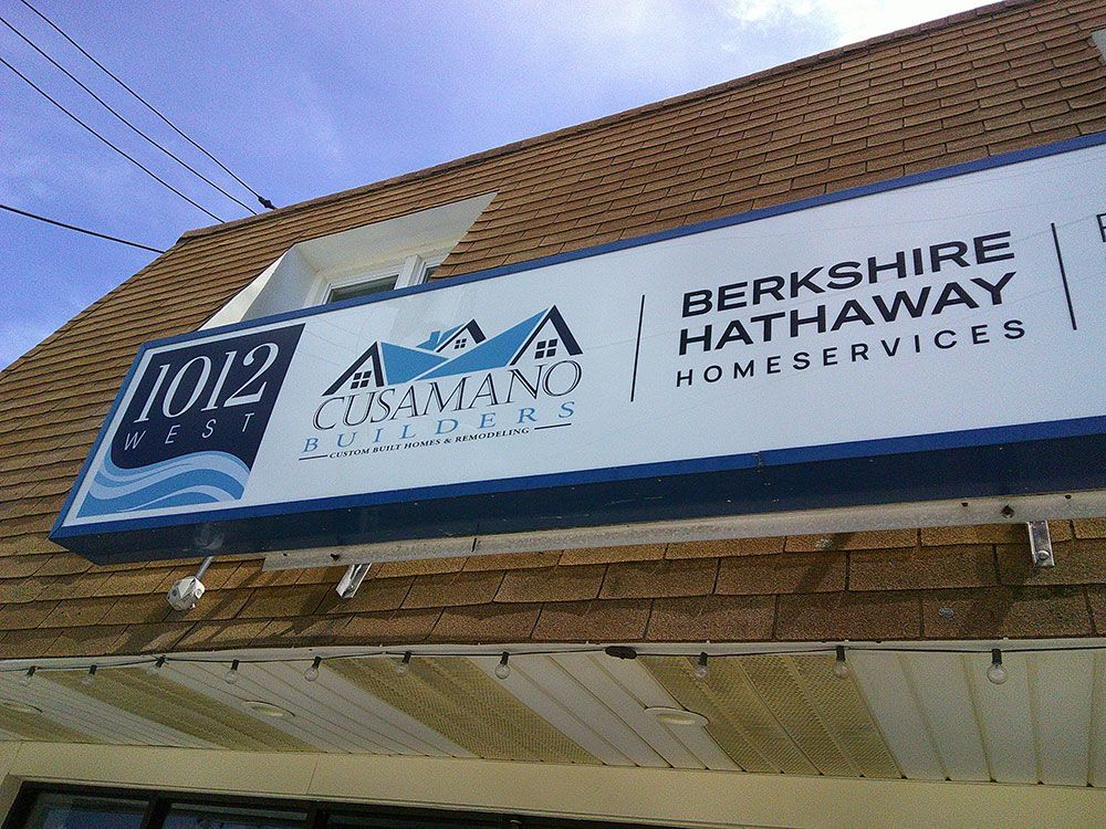 Sign for Berkshire Hathaway Homeservices and Cusimano Builders at 1012 West, white and blue on a brown roof.
