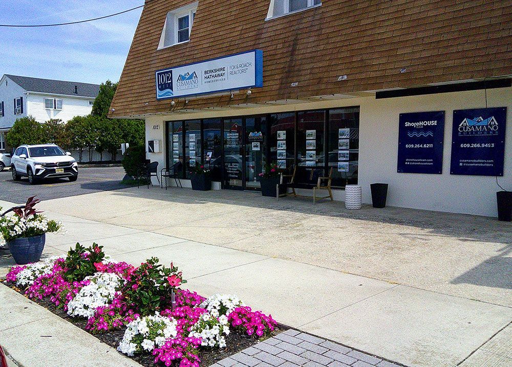 A real estate office with glass windows, flowers, and a car parked outside.