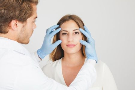 A doctor is examining a woman 's face with blue gloves.