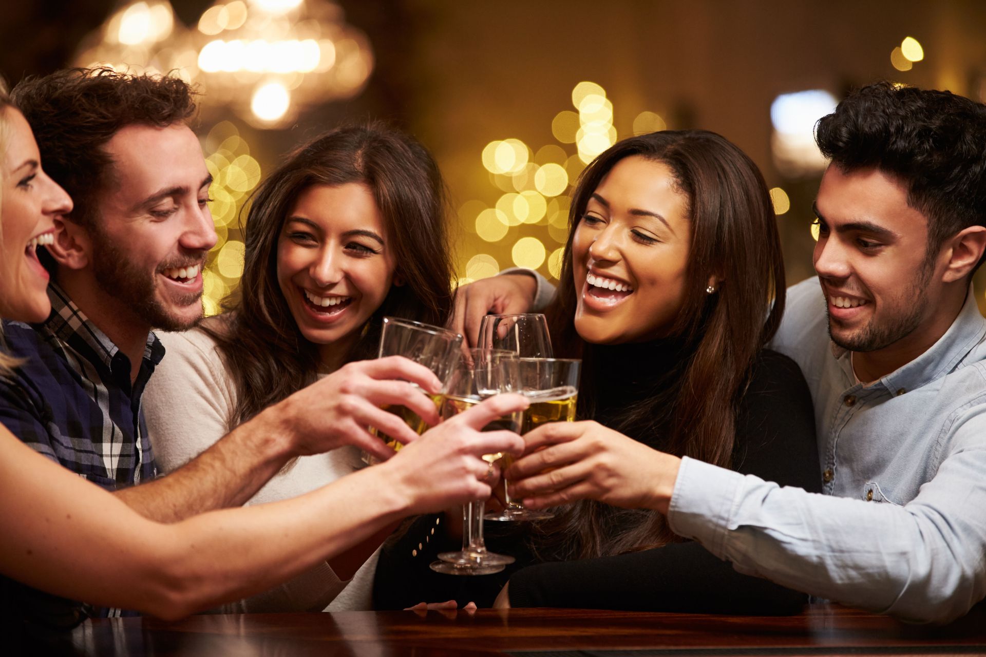 Friends toasting champagne glasses in a bar, illuminated by warm lights, smiling.