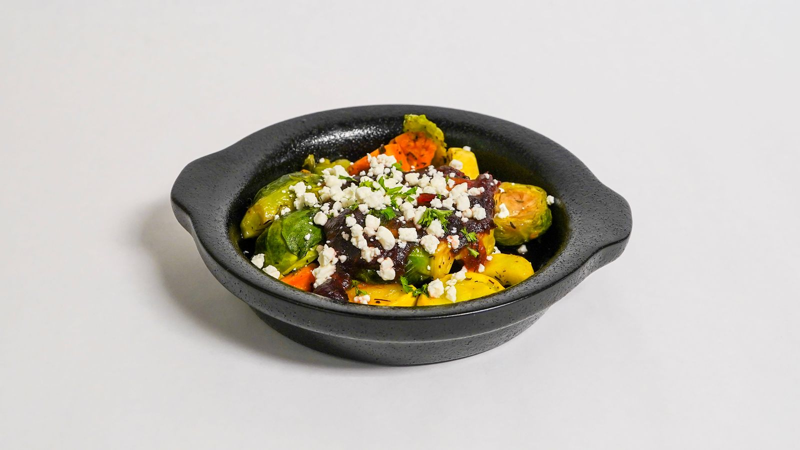 Roasted Brussels sprouts with toppings in a dark bowl on a white surface.