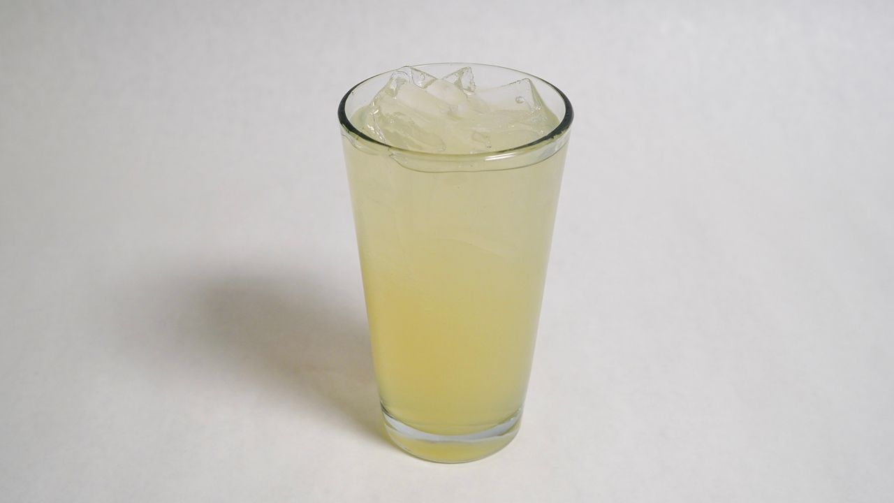 Tall glass of lemonade with ice on a white surface.