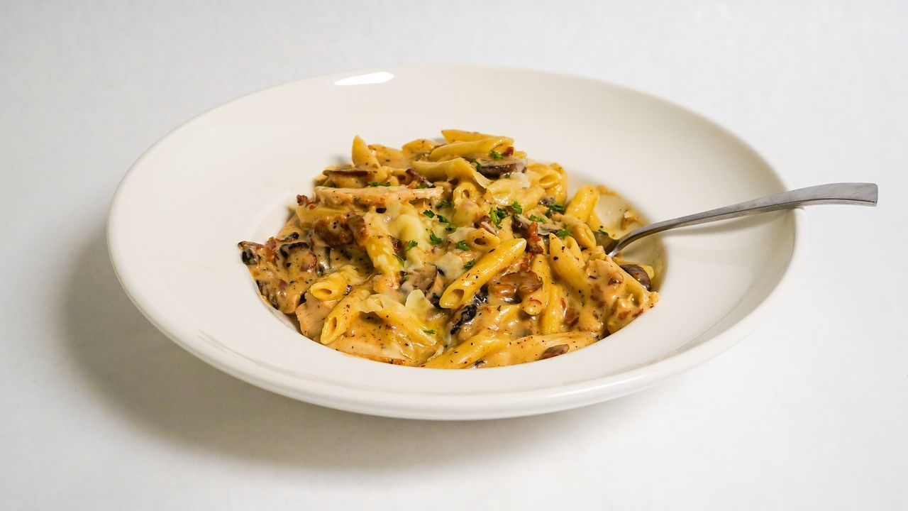Pasta dish in a white bowl with a fork on a white surface.