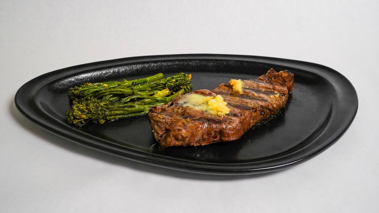 Grilled steak with butter, and asparagus on a black oval plate.