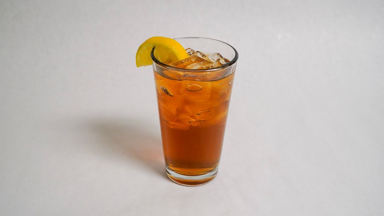 Tall glass of iced tea with ice and a lemon wedge.