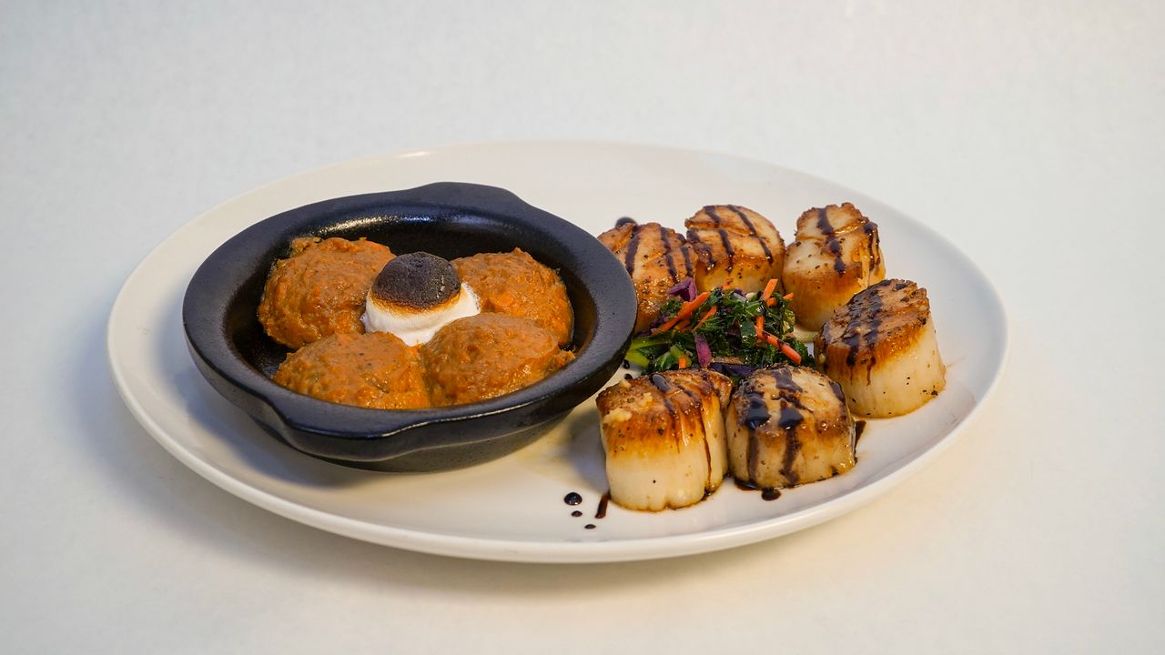 Plate with seared scallops and a side dish in a dark blue bowl.