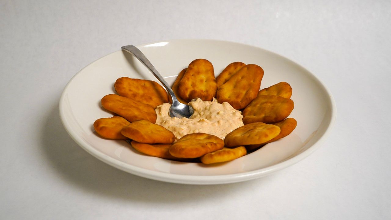 A plate of golden-brown fried food surrounds a dollop of tan dip; a spoon is in the dip.