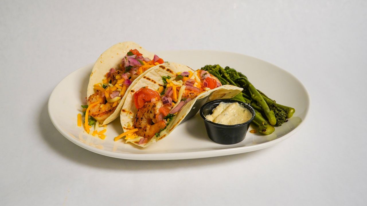 Three tacos with toppings, asparagus, and sauce on a white plate.