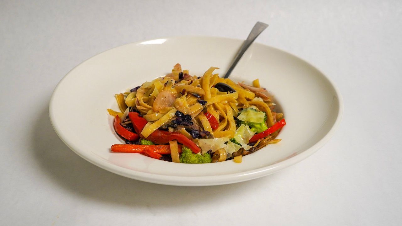 Salad with orange noodles, red peppers, broccoli, and a fork in a white bowl.