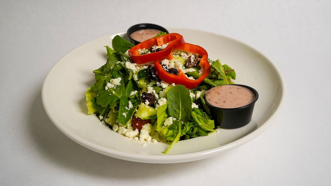 Salad with red pepper rings, olives, and feta cheese, served with two containers of dressing.