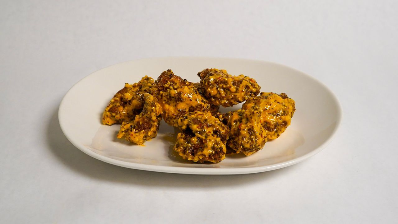 Chicken wings with golden sauce on a white oval plate.
