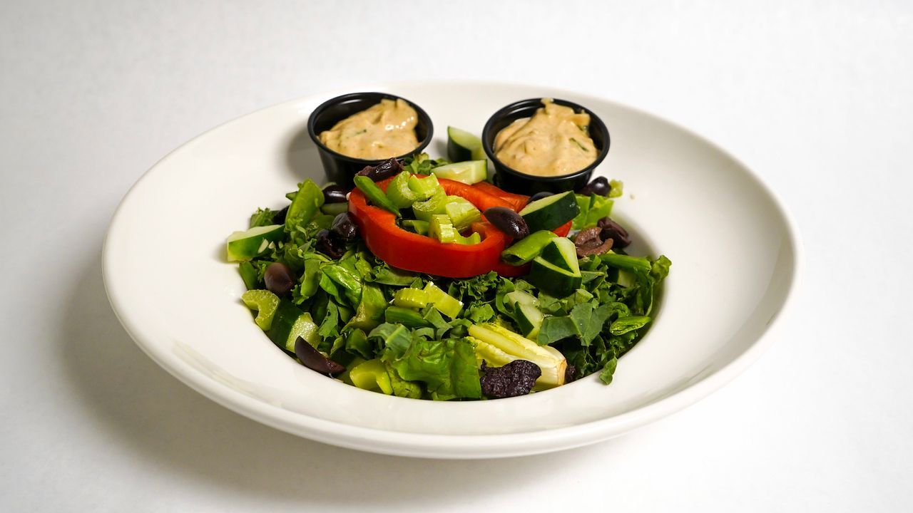 Salad with various vegetables, a red pepper, and two small dishes of sauce on a white plate.