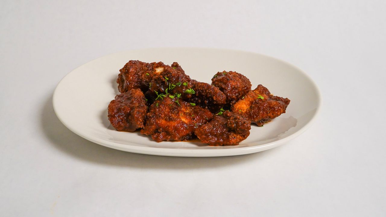 Plate of fried chicken pieces, coated in red sauce, garnished with herbs.