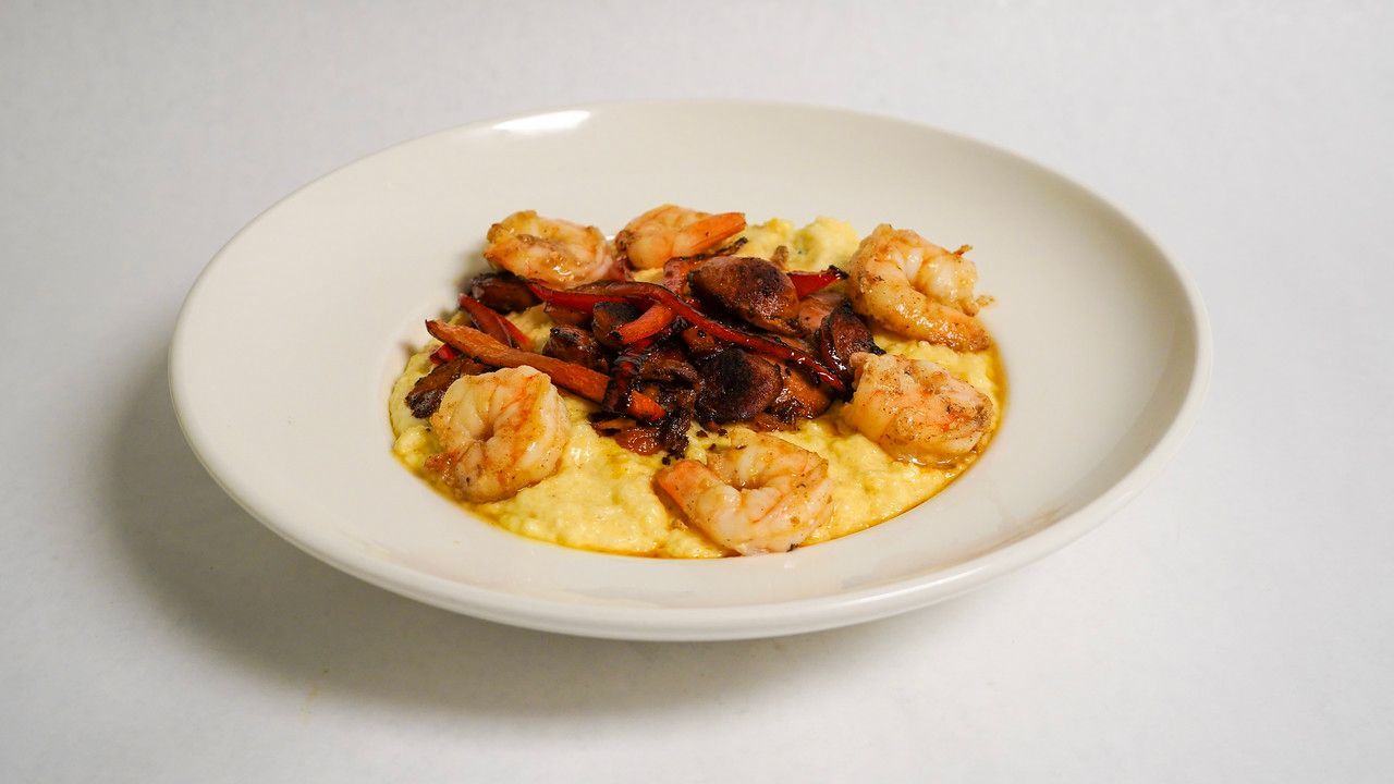 Shrimp and grits with red bell peppers, served in a white bowl.