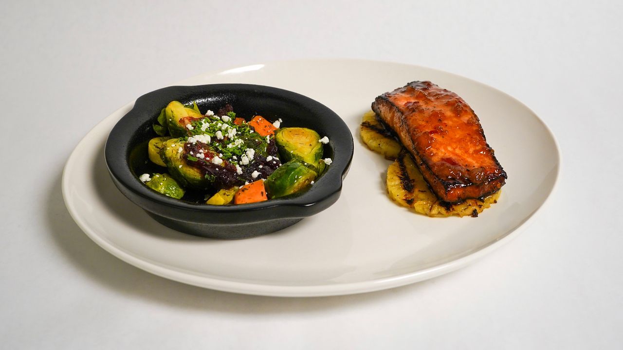 Salmon on pineapple with a side of vegetables in a black bowl on a white plate.