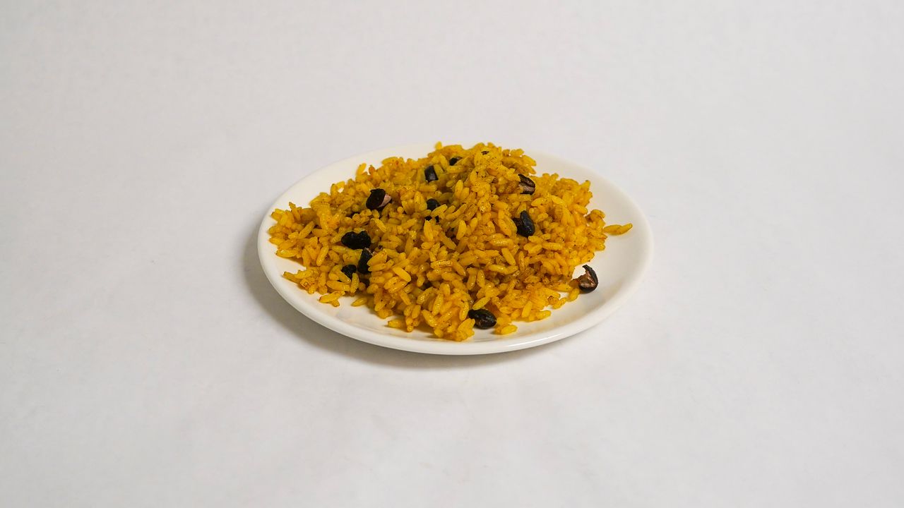 Yellow rice with dark beans on a white plate, set against a white background.