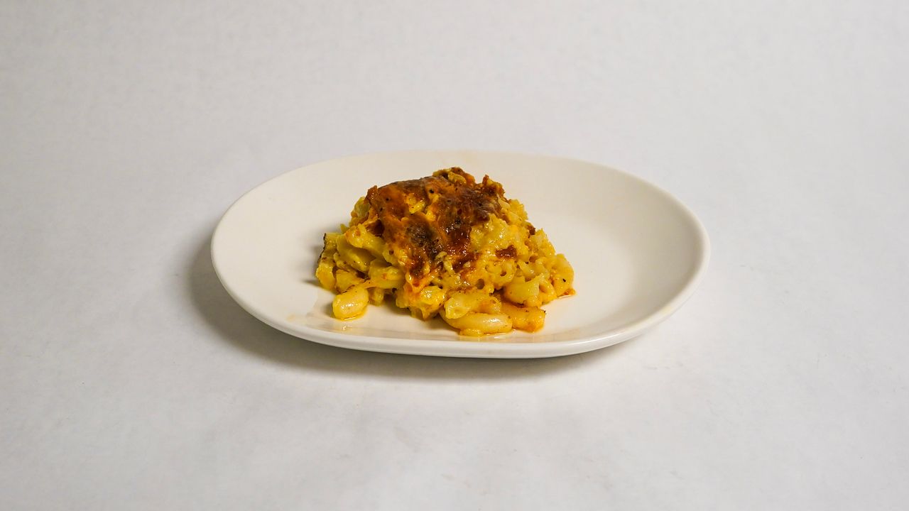 Macaroni and cheese on a white oval plate, topped with a brown crumbly topping, set on a white background.