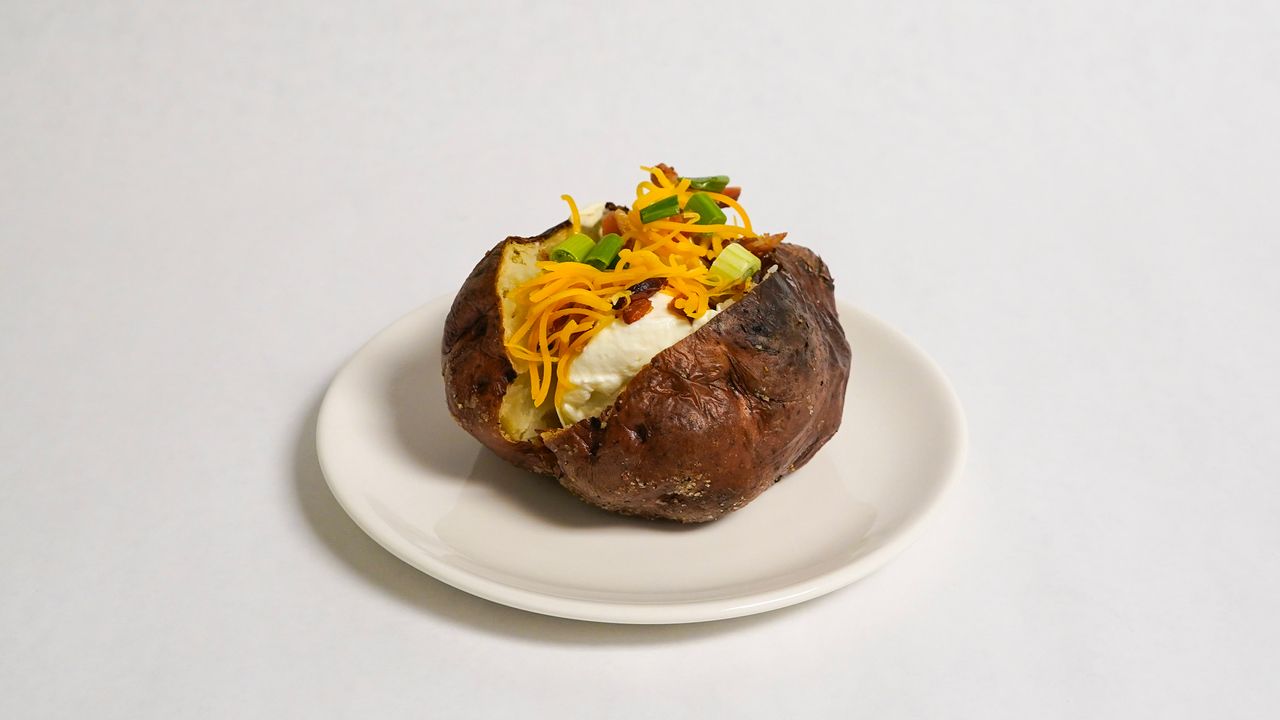 Baked potato topped with cheese, sour cream, and chives on a white plate.